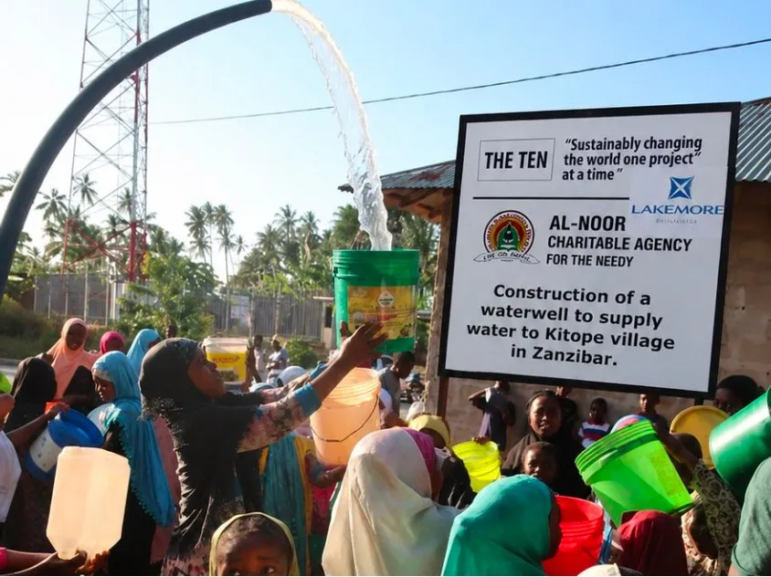 Villagers filling containers from a new waterwell in Kitope village, Zanzibar, beside the Al-Noor Charitable Agency project sign